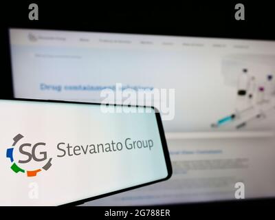 Telefono cellulare con logo della società italiana di vetro Stevanato Group S.p.A. su schermo davanti al sito. Mettere a fuoco al centro-sinistra del display del telefono. Foto Stock