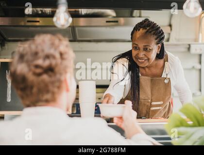 Donna chef africana che serve take away ordine all'interno del camion alimentare - Focus sul viso donna anziana Foto Stock