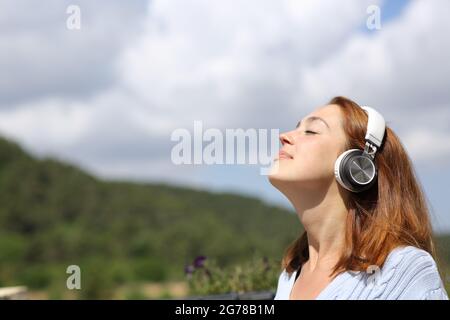 Donna rilassata che medita l'audio guida sulle cuffie respirando aria fresca in natura Foto Stock