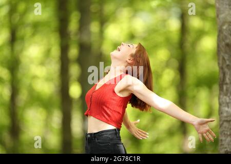 Profilo di una donna eccitata che stende le braccia urlando forte in una foresta Foto Stock