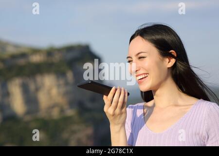 Felice donna asiatica sorridente utilizzando il riconoscimento vocale sul telefono cellulare in natura Foto Stock