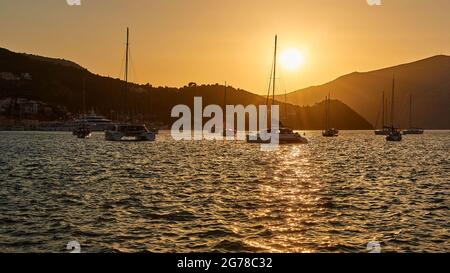 Isole IONIE, Ithaka, Baia di Molos, Vathi, crepuscolo, Tramonto, vista da Valthis sulla baia con barche a vela, sole sulle colline, cielo color sabbia, mare leggermente in movimento Foto Stock