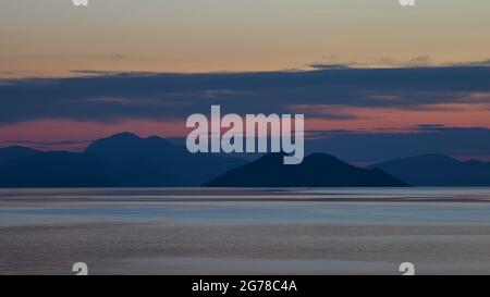 Isole IONIE, Ithaca, isola di Odysseus, Baia di Molos, Dawn, Vista dell'isolotto Skartsoubonisi, silhouette, vista della Grecia continentale, da rosa cielo a rosso, sopra le nuvole grigie, sopra cielo azzurro, grigio mare, calma Foto Stock