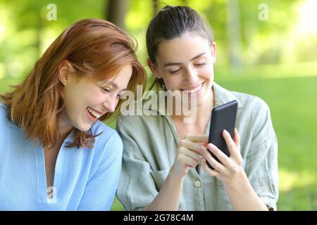 Due amici felici che ridono ad alto controllo smartphone in un parco Foto Stock