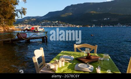 Isole IONIE, Ithaca, isola di Odysseus, capitale, Vathi, Baia di Vathi, taverna di pesce, barche da pesca, tavolo nel ristorante direttamente sull'acqua, palcoscenico di atterraggio all'ombra a metà distanza, Vathi sullo sfondo Foto Stock