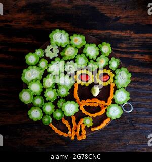 Vista dall'alto colorato melone amaro affettato, frutta verde e matura tagliata a fette pronta a cucinare sul tagliere su sfondo di legno scuro Foto Stock