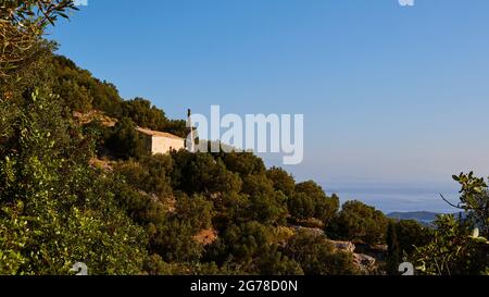 Isole IONIE, Ithaka, isola di Odysseus, Vathi, distretto di Perachori, si trova su un pendio boscoso di montagna, cappella a sinistra nella foto con alto campanile stretto, foresta tutto intorno, mare sullo sfondo, blu cielo Foto Stock