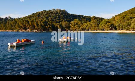 Isole IONIE, Ithaca, Isola di Odysseus, Vathi, Spiaggia di Loutsa, acqua verde, acqua blu, alberi sulla spiaggia, spiaggia solitaria, pedalò all'ancora, vista attraverso gli alberi Foto Stock