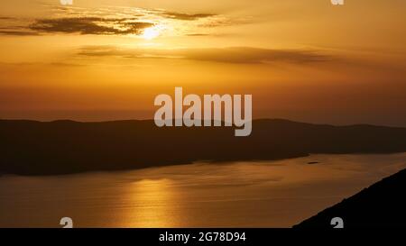 Isole IONIE, Ithaca, isola di Ulisse, tramonto su Kefaloniá, vista dalla costa occidentale di Ithaka attraverso lo stretto a Kefaloniá, tramonto dietro nuvole grigie in un cielo arancione, fascio di sole sul mare Foto Stock