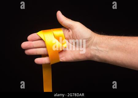 nastro giallo nel palmo della mano su sfondo nero; preparazione del nastro per l'imballaggio di un regalo. Foto Stock