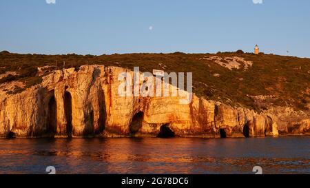 Isole IONIE, Zante, costa nord-orientale, Grotte Blu, Grotte Blu, Luce del mattino, costa rocciosa, faro, segno 'grotte blu', grotte in parete rocciosa, cielo blu, piccola luna nel cielo Foto Stock