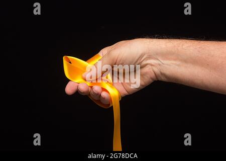 nastro giallo nel palmo della mano su sfondo nero; preparazione del nastro per l'imballaggio di un regalo. Foto Stock