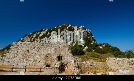 Isole IONIE, Zante, montagna vicino alla città di Zante, Monte Yves, monastero sulla cima, Panagia Skopiotissa, 15 ° secolo d.C., sorge sulle rovine di un antico tempio Artemide, cielo blu scuro, muro di pietra con porta ad arco a metà distanza, panchine del parco davanti ad esso, cime rocciose sullo sfondo Foto Stock