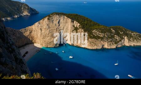 Zakynthos, Paralia Navagio, Shipwreck Beach, vista dall'alto verso e sopra la baia e la spiaggia parzialmente ombreggiata Navagio Beach, relitto MV Panagiotis all'ombra, escursioni barche all'ancora, barche a vela all'ancora, acque blu e turchesi, senza cielo Foto Stock