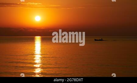 Zante, città di Zante, luce del mattino, umore del mattino, alba sul mare, il sole sorge in alto a sinistra della foto, barca da pesca si sposta da destra a sinistra, riflesso del sole sull'acqua Foto Stock