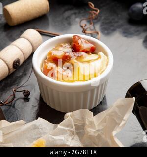 Miele in vaso su tavola di pietra scura con cavatappi di formaggio di vino in nero uva succosa cornice. Delizioso miele di ape gialla mescolato con noci e frutta secca Foto Stock