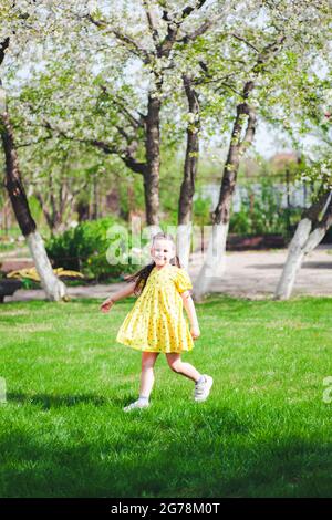 una ragazza felice di sei anni corre su un prato verde nel parco e ha un buon tempo, attività in famiglia nel fine settimana Foto Stock