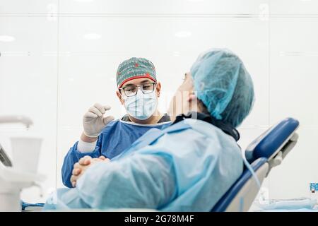 Medico di sesso maschile indossando indumenti protettivi e maschera facciale che parla con paziente non riconosciuto in clinica. Foto Stock