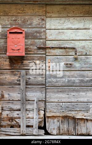 La cassetta postale rossa appesa su una vecchia porta esterna in legno Foto Stock