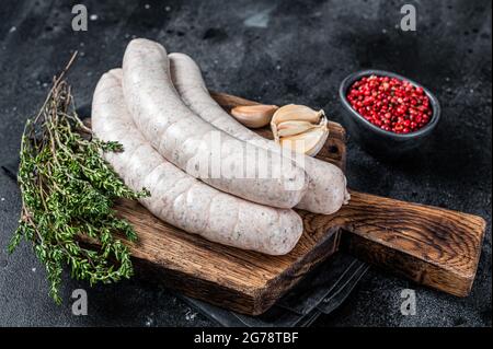 La salsiccia bianca cruda di Monaco weisswurst su tavola di legno. Sfondo nero. Vista dall'alto Foto Stock