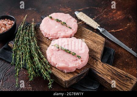 Hamburger crudi freschi cotoletta di pollo e carne di tacchino con erbe. Sfondo scuro. Vista dall'alto Foto Stock