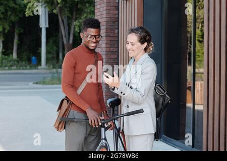 Felice uomo d'affari con smartphone che mostra nuova app mobile per l'uomo africano con bicicletta Foto Stock