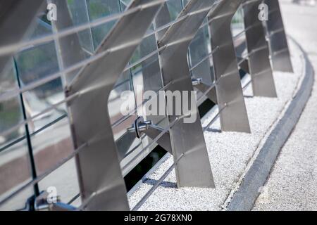 tenditori in metallo fissaggio di cavi con asta in acciaio su ponte pedonale con percorso in ciottoli e barriera in vetro per dettagli di sicurezza ravvicinati dei coni Foto Stock