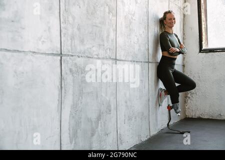 Giovane sportivo con protesi sorridente mentre si appoggia alla parete interna Foto Stock