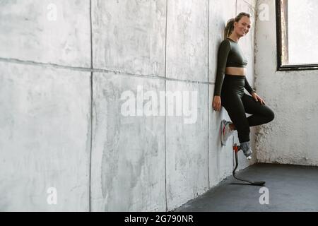 Giovane sportivo con protesi sorridente mentre si appoggia alla parete interna Foto Stock