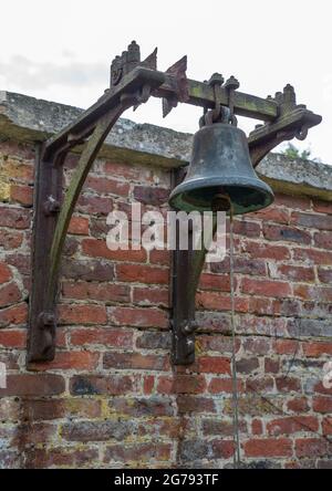 Una grande campana montata su una parete di mattoni con lavoro metallico e corda di trazione Foto Stock