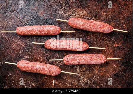 Kebab crudo di carne kofta salsicce su spiedini. Sfondo scuro. Vista dall'alto Foto Stock