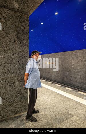 U Museumsinsel, Unter den Linden, Mitte, Berlin.with uomo anziano che indossa il facemark durante la corona Pandemic. La nuova stazione ferroviaria metropolitana progettata dall'architetto Max Dudler ha aperto il 9 luglio 2021. Dudier è stata ispirata da Friedrich Schinkel che ha progettato la May degli edifici storici della zona. Il soffitto della stazione, un cielo stellato, si riferisce ad una decorazione che Schinkel progettò nel 1816 per una rappresentazione del ‘Flauto Magico’ di Mozart. Il cielo in un blu profondo e 6662 luci creano le stelle. Foto Stock