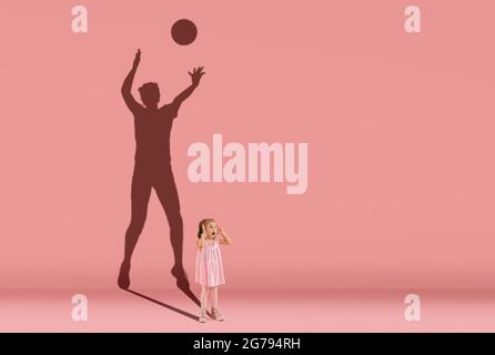 Infanzia e sogno sul grande e famoso futuro. Immagine concettuale con la bambina e l'ombra del giocatore di pallavolo femminile sulla parete rosa corallo Foto Stock