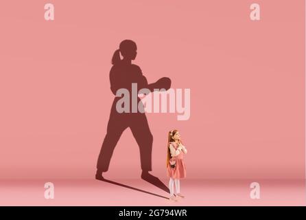 Infanzia e sogno sul grande e famoso futuro. Immagine concettuale con la ragazza e l'ombra di forte praticante taekwondo femminile sul rosa corallo Foto Stock