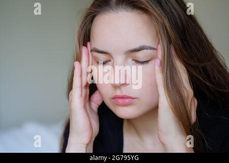 Ritratto di bella giovane donna che soffre di mal di testa disperata e stressata perché dolore ed emicrania, sensazione di malessere, mani sulla testa Foto Stock