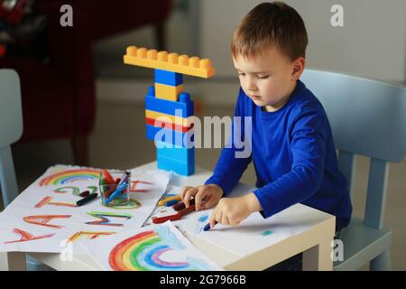 Un ragazzo di 4-7 anni si siede al tavolo e disegna con vernici multicolore. Creatività dei bambini. Hobby per bambini. Foto di alta qualità Foto Stock