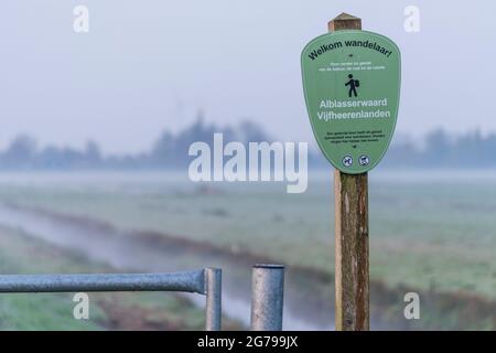 Impressioni di un'escursione primaverile all'alba e alla nebbia nell'Olanda del Sud nella regione di Alblasserwaard Vijfheerenlanden vicino a Kinderdijk: Indicazione per il percorso escursionistico 'Welkom Wandelaar' - gli escursionisti sono i benvenuti Foto Stock