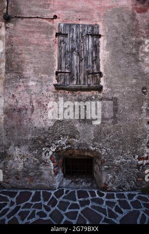 Moderno pavimento in lastre di pietra di fronte ad un'antica parete di casa con persiane chiuse, Anfo sul Lago d'Idro Foto Stock