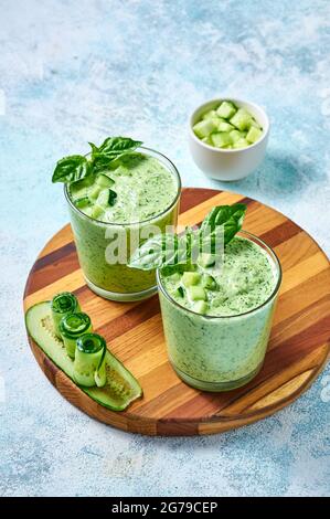 Cetriolo Gazpacho - zuppa estiva fredda con basilico in bicchieri su tavola di legno su sfondo chiaro. Foto Stock