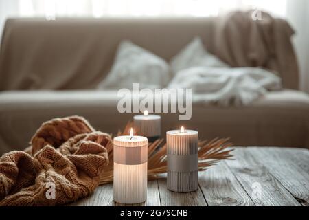 Accogliente composizione domestica con candele brucianti su un tavolo di legno con un elemento a maglia. Foto Stock