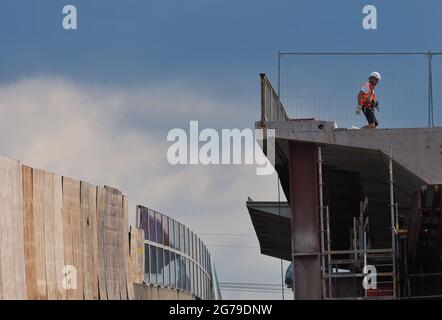 12 luglio 2021, Brandeburgo, Potsdam: Un lavoratore cammina lungo uno dei segmenti del vecchio ponte nel cantiere del ponte sopraelevato della strada statale L40 Nuthestrasse. A causa di una mancanza di spazio, i tratti di cemento e acciaio di rinforzo lunghi circa 30 metri e 600 tonnellate vengono tirati in diversi passaggi parziali dietro il moncone Friedrich-Engels-Strasse utilizzando l'impianto idraulico, dove la vecchia sovrastruttura viene frantumata e trasportata via. La ristrutturazione del ponte stradale sopraelevato è prevista per il completamento nell'ottobre 2022. Foto: Soeren Stache/dpa-Zentralbild/ZB Foto Stock