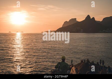 Un luogo magico: La gente applaude quando il sole tramonta alla roccia di Arpoador con vista della spiaggia di Ipanema e le montagne di Morro Dois Irmaos e Leblon nella parte posteriore. Macchina fotografica: Leica M10 Foto Stock