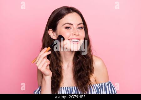 Foto di bella ottimista bruna donna applicare make up indossare abito blu isolato su sfondo di colore rosa Foto Stock