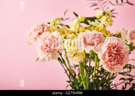 Bouquet di garofani rosa e mattiola gialla con rami verdi. Design concetto di saluto per le vacanze con bouquet di garofano su sfondo rosa. Foto Stock