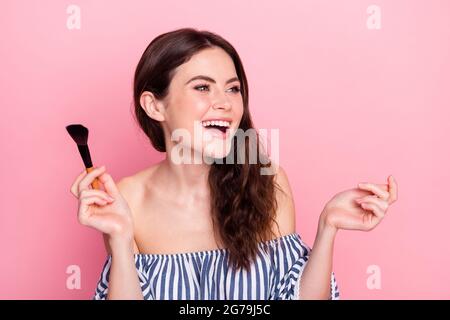 Foto di bella ottimista bruna signora applicare make up look spazio vuoto indossare abito blu isolato su sfondo di colore rosa Foto Stock