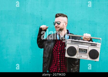 Uomo bearded che ascolta la musica con stereo e balli boombox vintage Outdoor contro una parete blu - Cool uomo divertirsi ballare in strada con un vin Foto Stock