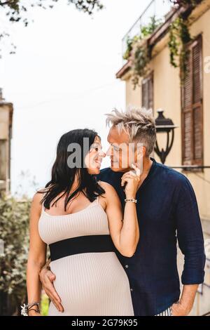Felice coppia, con donna incinta, guardando gli occhi l'un l'altro e posando per una foto durante la vacanza estiva in un villaggio - giovane moglie e marito Foto Stock