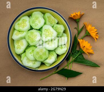 Succulenta insalata di cetrioli crudi in un piatto su un tavolo di legno con fiori gialli. Foto Stock