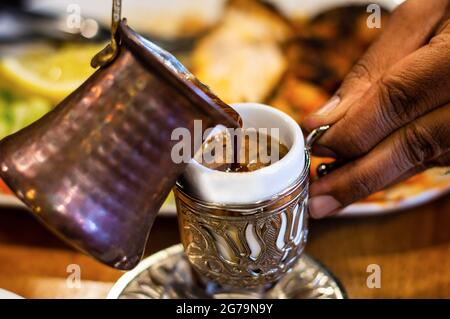 Versare il caffè turco in una tazza tradizionale in metallo goffrato Foto Stock