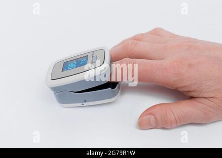 Un braccio di una donna anziana sta misurando da vicino i livelli di ossigeno nel sangue con il dito in un pulsossimetro su sfondo bianco. Foto Stock